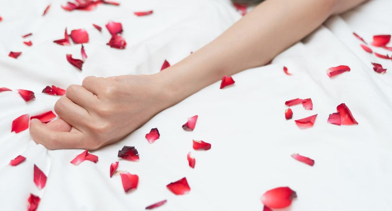 mano su lenzuolo coperto da petali di rosa, un modo per far impazzire una donna a letto